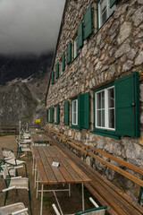 Sideview of the Südwandhütte and an empty terrace with wooden tables waiting for tourists under a dark moody and rainy sky.