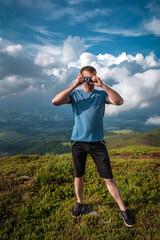 Fototapeta na wymiar Man in blue shirt makes pictures on film retro camera in mountains