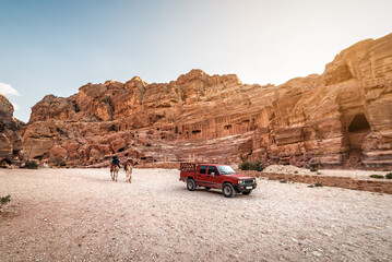 Red off-road car and two camels in Petra city. Jordan