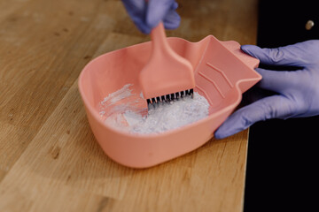 Cropped photo of woman colorist wearing blue rubber gloves, mixing hair dye color in bowl with...