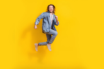 Fototapeta na wymiar Full length photo of impressed funny man wear denim jacket smiling jumping high isolated yellow color background
