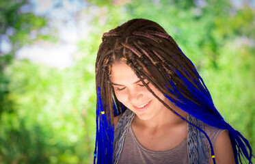 A girl with dreadlocks smiles while walking in the park. A woman with a creative hairstyle has fun...