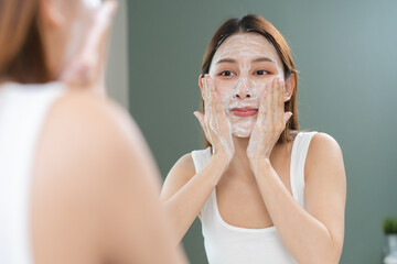 facial skin care routine concept. young woman looking in the mirror during washing her face with...