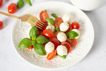 Italian caprese salad with sliced tomatoes, mozzarella, basil, olive oil on a light background.