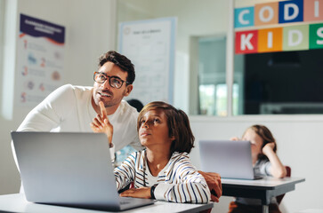 Teacher helping a young student with a coding exercise in a computer literacy class