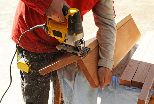 Carpintero ajustando con una sierra caladora un escalón de madera de haya de una escalera interior para una casa de dos plantas