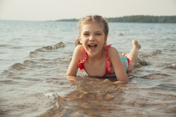 laughing girl of 5 years in blue swimsuit lies on shore in sea water
