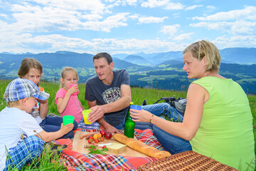 Junge Familie mit Kindern beim Picknick in sommerlicher Gebirgslandschaft