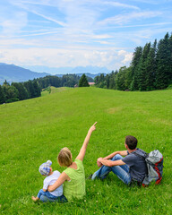 Junge Familie genießt die herrliche Landschaft in den Alpen auf einer Wiese sitzend