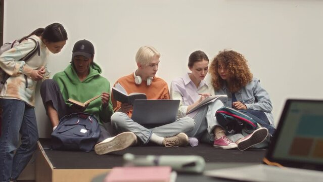Slowmo of young multicultural first year university or college students working on project together sitting on floor in bright modern campus