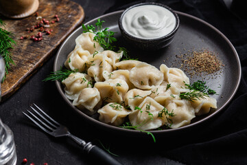 Dumplings with sour cream and herbs on a dark plate. Meat dumplings
