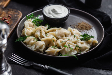 Dumplings with sour cream and herbs on a dark plate. Meat dumplings