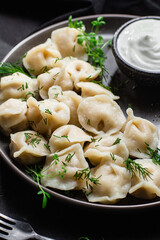 Dumplings with sour cream and herbs on a dark plate. Meat dumplings