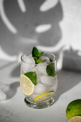 Summer refreshing cocktail Mojito with rum, mint, lime and ice in glass on a grey background and shadow on a wall.