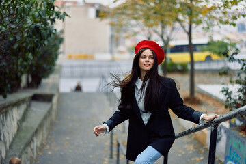 Fashion woman walking down steps against city backdrop in stylish clothes with red lips and red beret, travel, cinematic color, retro vintage style, urban fashion lifestyle.