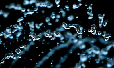 Drops of water splash blue water on a black background, concept of freshness drink, watering the rain source of pure water fountain copy space