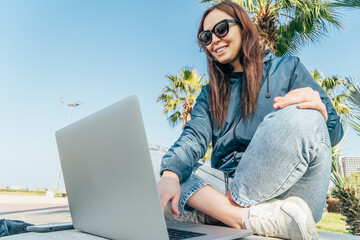 Young woman sitting in park with legs crossed, using laptop for video call.