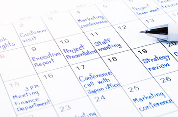 The handwriting scheduling appointments on calendar sheet with pen.