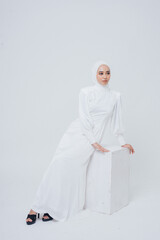 Woman model with white hijab and white dress pose in studio. She's pose in white background studio. She's like look beautiful and graceful. She's the one of the many model in Indonesia.