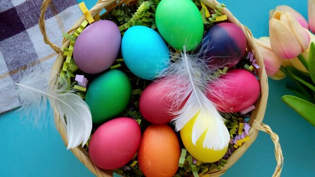 White feather falls on a basket of colored Easter eggs top view closeup