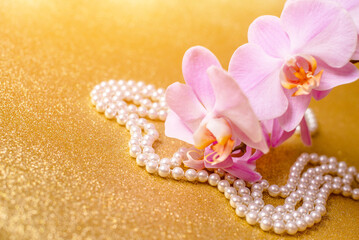 purple Orchid and pearl necklace on a shiny gold background
