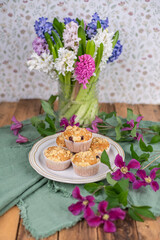 Tischdekoration im Frühling mit frischen Blumen und Muffins, Blumenstrauß und Gepäck auf einem Tisch