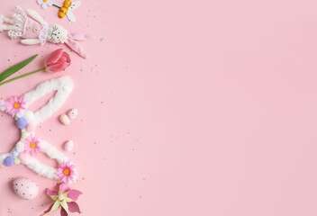 cute easter composition. bunny ears, painted eggs, flowers, confetti and a toy bunny on a pastel pink background. top view. copy space. flat lay. place for text