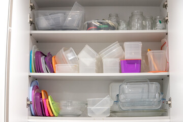 Open kitchen cupboard full of plastic and glass containers inside.