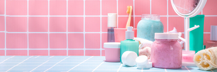 Bath background with cosmetics, cream, scrub, toothbrush, serum, mirror pink and blue tiled bright background. Cute bright self care, spa, relax, time for yourself concept