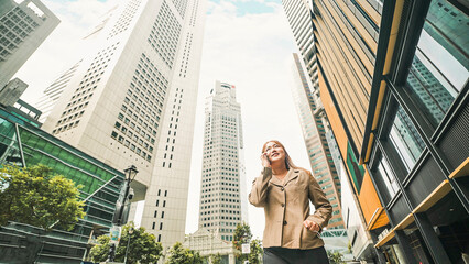 Happy young business woman walking in city street and speaking with smartphone