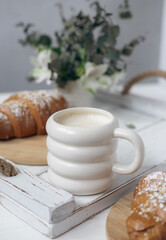 A cup of aromatic cappuccino and a croissant on a white tray