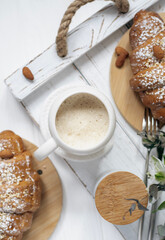 A cup of aromatic cappuccino and a croissant on a white tray