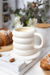 A cup of aromatic cappuccino and a croissant on a white tray