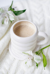 A cup of cappuccino and flowers on a white knitted background