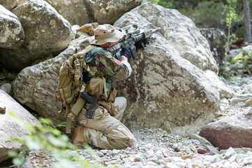 Homme militaire en uniforme à couvert derrière un gros rocher de granit. Rechargement d'arme, fusil, viseur, tir