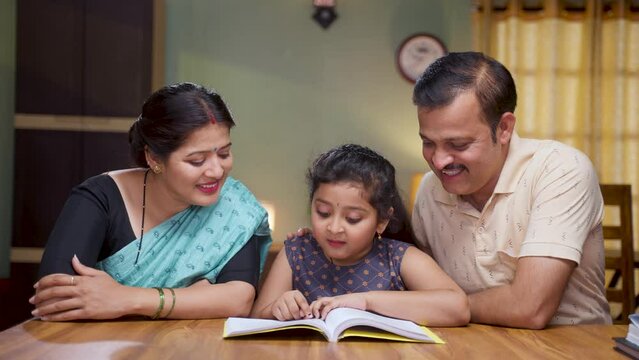 Couple got happy by seeing little girl daughter confidently reading book at home - concept of intelligence, family caring and education