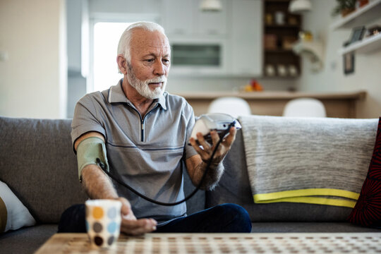 Caucasian man taking his own blood pressure. Active senior man measuring blood pressure with sphygmomanometer in living room.
