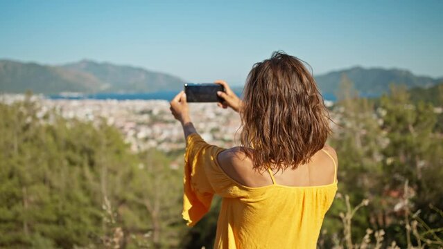 rear view woman traveler photographer makes selfie or video call standing on background of Marmaris, beautiful sea bay with clear turquoise water. slow motion, travel in Turkey