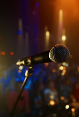 Let music fill the air...A microphone standing on a stage with a crowd in the background.