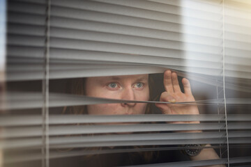 Blond man peeking through window blinds
