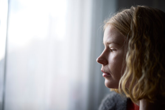 Pensive teenage girl looking through window