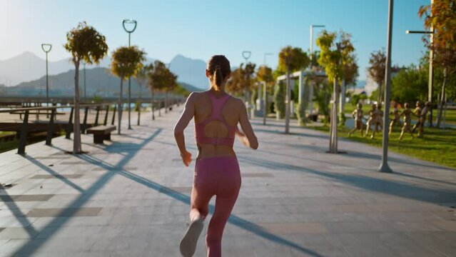 back view treking camera shot Young fitness sports woman running outdoors on the promenade during sunset