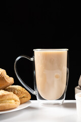 Tea with milk in a glass cup with a double bottom and cakes on a black background, place for text