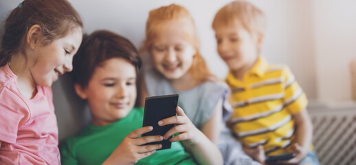 Fototapeta premium Group of children sitting indoors and looking in the smartphone