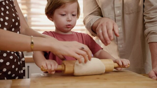 Father and mother teaching son kneading dough in home kitchen, family relations concept
