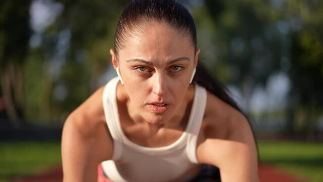 Close-up portrait of confident concentrated sportswoman raising face looking at camera in slow motion on starting line. Front view Caucasian fit motivated woman posing on sports track at sunset
