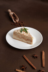 Layered Cake with cream Napoleon with mint on Brown background. A cinnamon stick, badyan, coffee beans on a brown background. Copy space