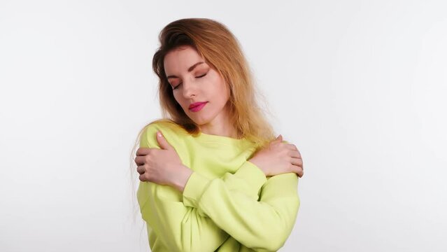 Young woman embracing herself, hugging self-love, smiling. Positive joyful lady in yellow sweatshirt, narcissistic egoistic complacency emotion. Indoors studio, isolated on white background