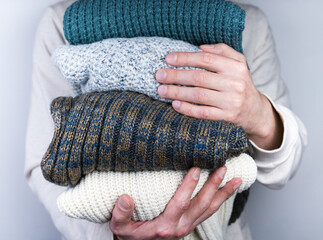 A young man holds warm knitted sweaters in her hands. Warm winter clothes. Selective focus.