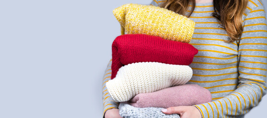 A young girl holds multi-colored knitted warm sweaters in her hands. Autumn and winter clothes. Banner. Copy space. Selective focus.